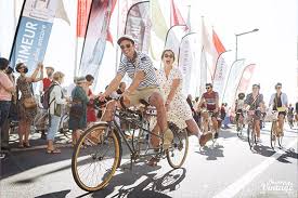une femme et un homme sur un velo qui passe devant une foule